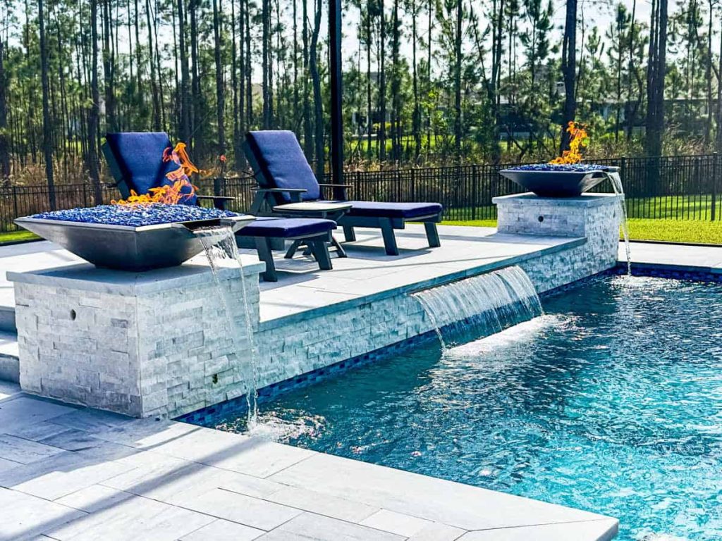 Elegant pool with luxury pool features Tampa, lounge chairs, and fire bowls in a backyard setting.