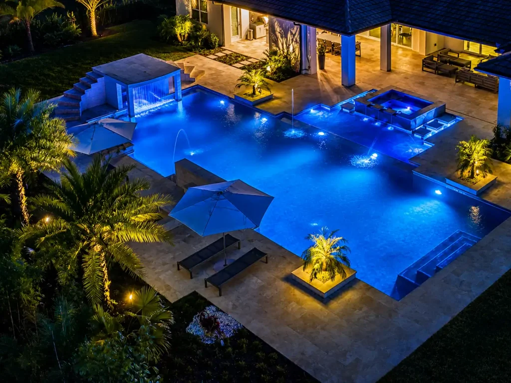 Night view of a luxurious illuminated pool with seating and waterfall features in luxury pool features Tampa